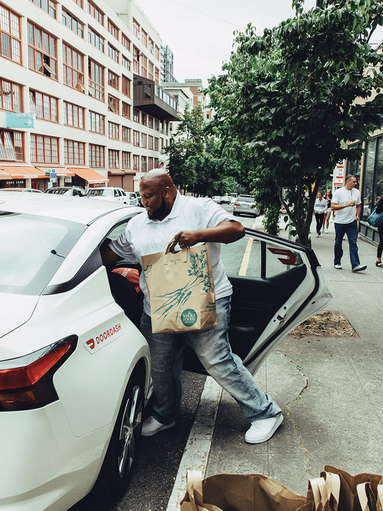 Man loading DoorDash car with grocery bag for delivery