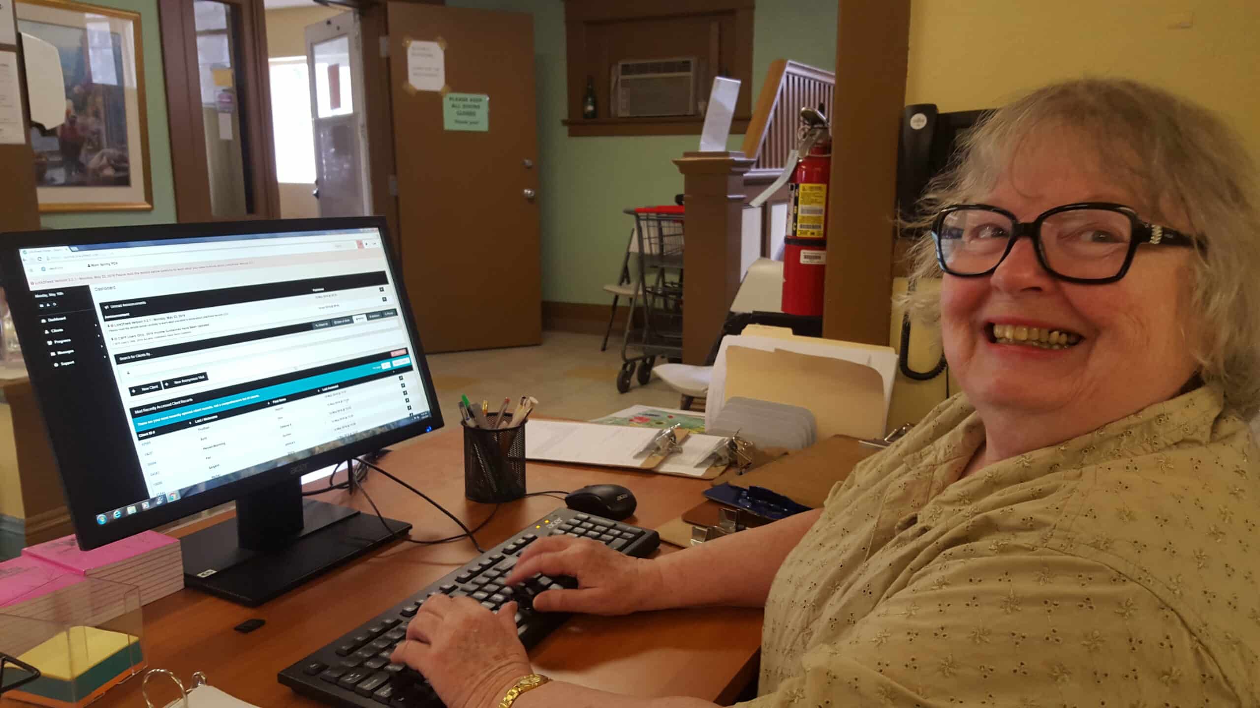 Woman smiling sitting at a desk using Link2Feed Case Management Software at United Way