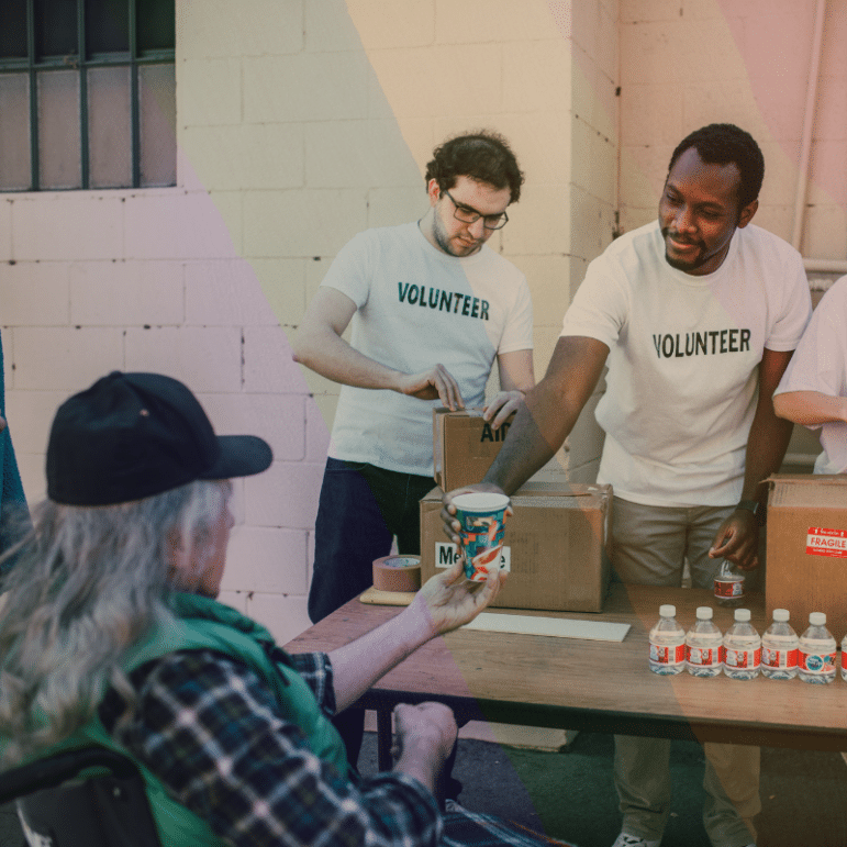 Two volunteers handing out food to an elderly man in a wheelchair.