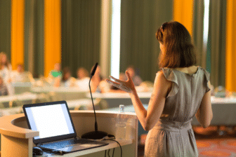 A woman standing in front of a laptop and giving a presentation.